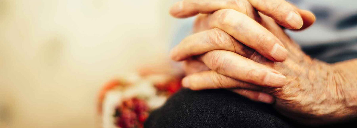 An older patient living with non-small cell lung cancer (NSCLC) with their hands clasped together in their lap.