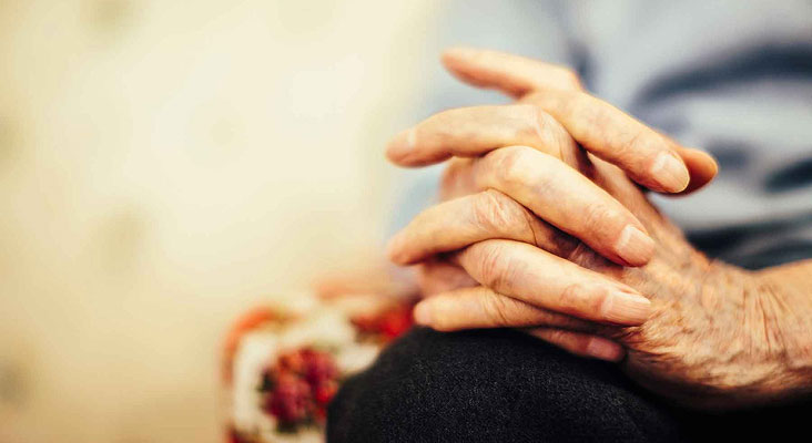 An older patient living with non-small cell lung cancer (NSCLC) with their hands clasped together in their lap.