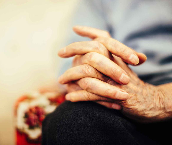 An older patient living with non-small cell lung cancer (NSCLC) with their hands clasped together in their lap.