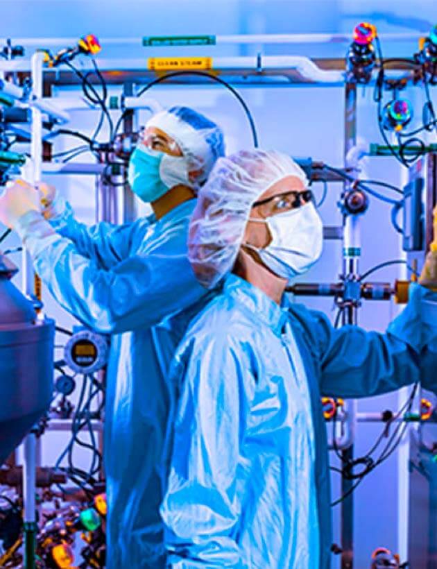 Two scientists with lab coats and masks working in a lab together.